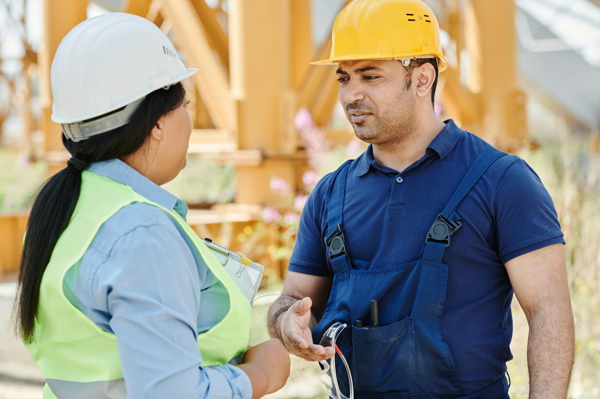 Male and female construction workers discussing safety on a sunny day outdoors.